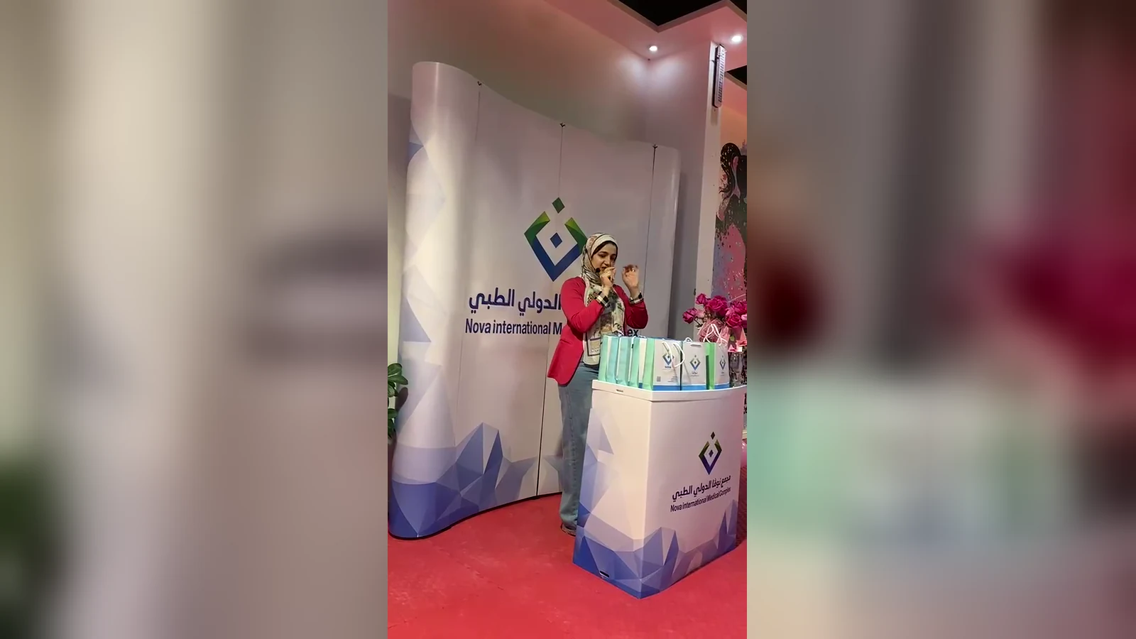 ركن مجمع نوفا الدولي الطبي في فعالية أكتوبر الوردي، وأمامه منصة عليها أكياس الهدايا وباقة ورود وردية