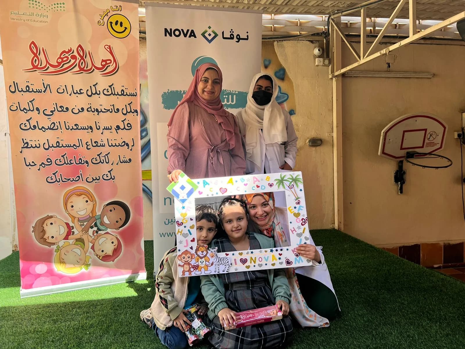 عضوة من فريق نوفا مع طفلين من الروضة يحملون إطار صور مزيّناً